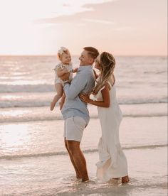 a man and woman holding a baby on the beach