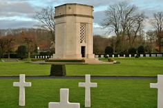 a cemetery with crosses in the grass and a tower behind it on a cloudy day