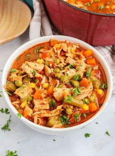 a white bowl filled with chicken and vegetable soup next to a red pot full of stew