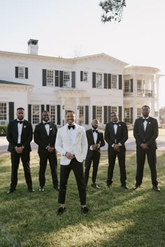 a group of men in tuxedos posing for a photo on the grass near a large white building