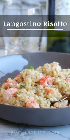 a bowl filled with rice and shrimp on top of a table next to a bottle of wine