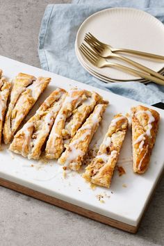 a white plate topped with sliced pastries on top of a wooden cutting board next to a knife and fork