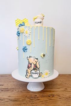 a winnie the pooh birthday cake with flowers and honey on top, sitting on a wooden table