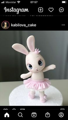 a small white rabbit figurine with pink tutu skirt and bow on it's head