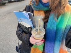 a woman is holding a drink and looking at her cell phone while standing on the street