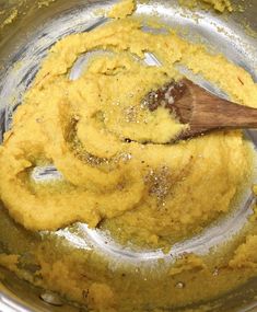 a wooden spoon mixing some yellow food in a pot with other ingredients on the side