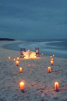 a table set up on the beach with lit candles