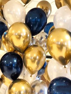 a bunch of balloons that are gold and white with some blue on them in the air