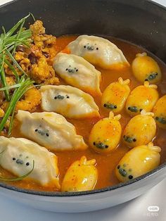 some dumplings are being cooked in a pan with sauce and herbs on the side