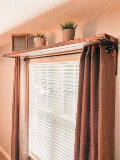 a window with curtains and plants on top of it in front of a white wall