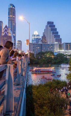 people are standing on the edge of a bridge overlooking a river with boats in it