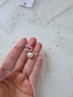 a hand holding a pearl and mesh ring on top of a white cloth covered table