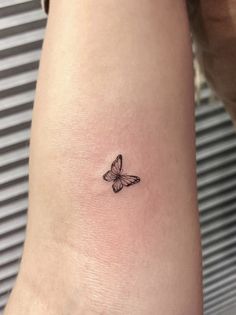 a small butterfly tattoo on the wrist is shown in black and grey colors, with an outline of a butterfly