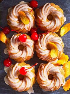 several donuts with frosting, cherries and oranges on a table top