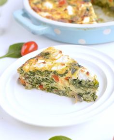 a slice of quiche on a plate next to a dish with tomatoes and spinach