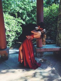 a man and woman are kissing in front of some pillars with trees behind them on a sunny day