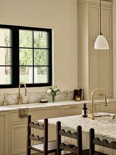 a kitchen with marble counter tops and wooden chairs in front of a window that has black framed windows