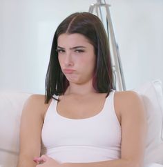 a woman sitting on top of a white couch with her hand on her stomach and looking at the camera