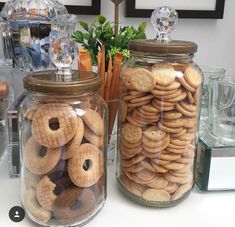 two glass jars filled with cookies and pretzels on top of a white counter