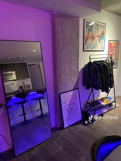 a room with purple lighting and clothes hanging on racks in front of the mirror that is lit up