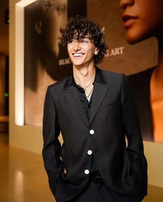 a young man in a black suit standing next to a wall with a movie poster behind him