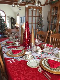 a dining room table set for christmas with plates and silverware on the placemats