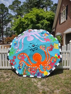 an octopus umbrella sitting on the grass in front of a white picket fence and house