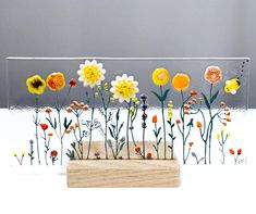 a wooden block with flowers on it sitting in front of a gray wall and grey background