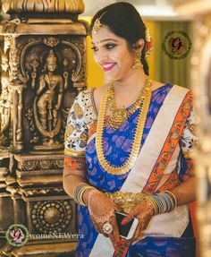 a woman in a blue and orange sari with gold jewelry on her neck standing next to a statue