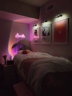 a bed in a room with pink lights on the wall and posters above it,