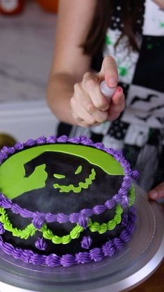 a woman decorating a halloween cake with green and purple icing