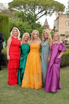 four women in colorful dresses posing for a photo on the lawn at a formal event