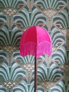 a pink table lamp with fringe on it in front of a wallpapered background