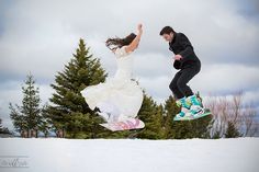 a man and woman jumping in the air on their snowboards with trees behind them