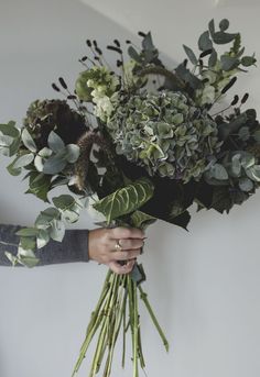 a person holding a bunch of flowers in their hands with greenery on the stems