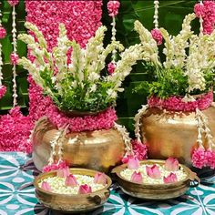 pink and white flowers are in gold vases on a table with blue and white tile