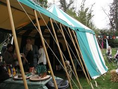 several people are standing in front of a tent with food and drinks on the table