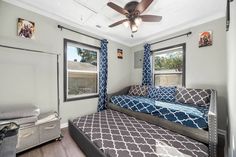 a bedroom with a bed, ceiling fan and window in the room that has blue curtains on it