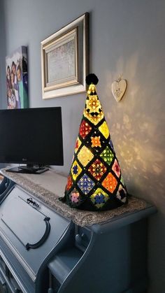 a colorful crocheted christmas tree sitting on top of a dresser next to a tv