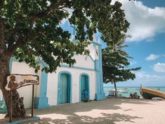 a white and blue building with a tree in front of it on the beach next to water