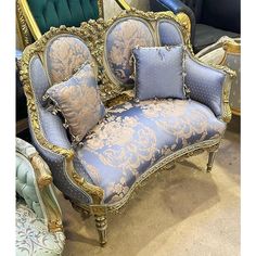 an ornate couch with blue and gold fabric on it's back, sitting in front of a green velvet upholstered chair