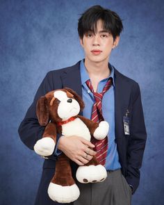 a young man holding a stuffed dog in his hands and wearing a suit with a tie