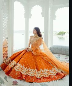 a woman sitting on top of a bed wearing an orange and white dress with gold accents