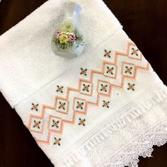 a white towel with flowers on it sitting on a wooden table next to a vase