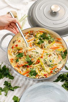 a person holding a spoon in a pan filled with noodles and vegetables on a table