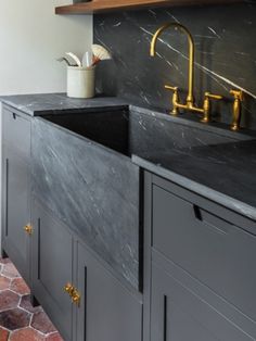 a kitchen with black counter tops and gold faucets on the sink, along with marble flooring