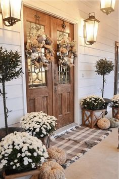 the front porch is decorated for fall with white mums and potted plants on either side