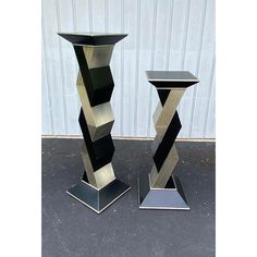 two black and silver vases sitting next to each other on top of a cement floor