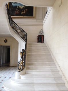 a white staircase with black handrails leading up to a painting on the wall