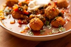 a white plate topped with meatballs covered in sauce and toppings on top of a wooden table